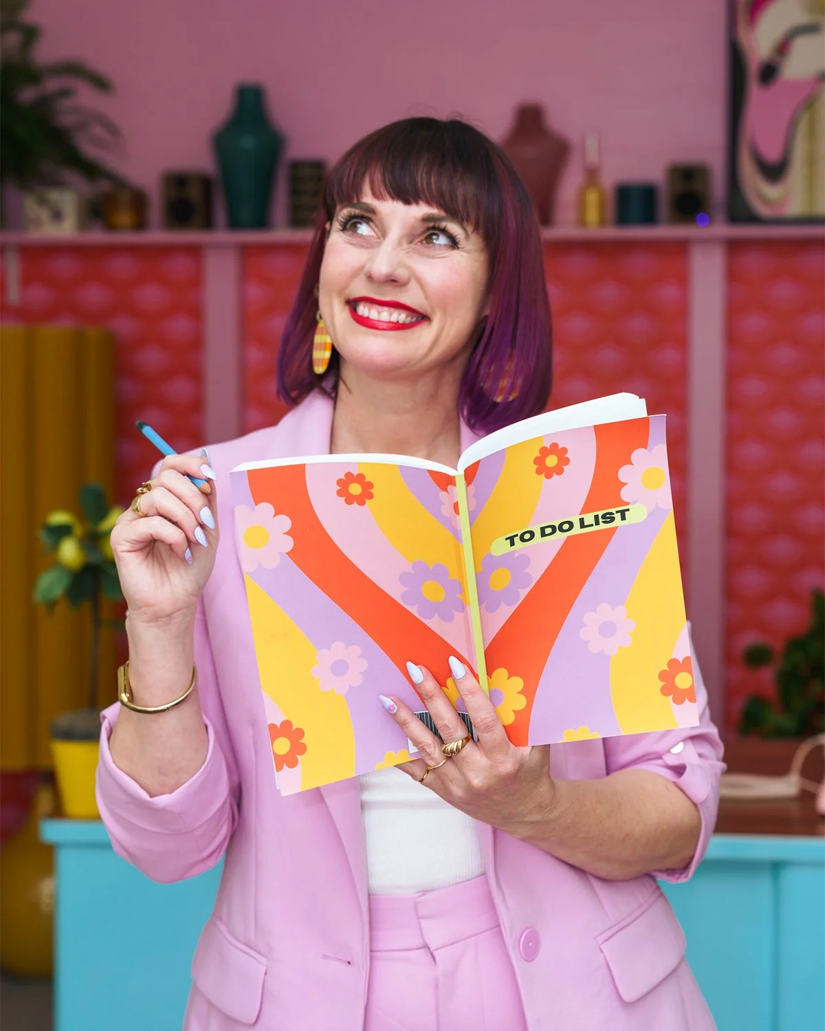 Taryn, a white woman, smiling, looking up, while standing writing in colorful to do list notebook.
