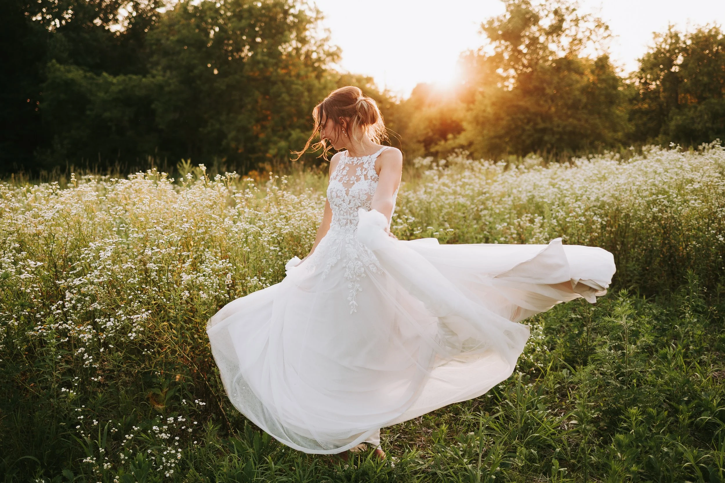 A woman in a white wedding dress standing in a field of white flowers at sunset.