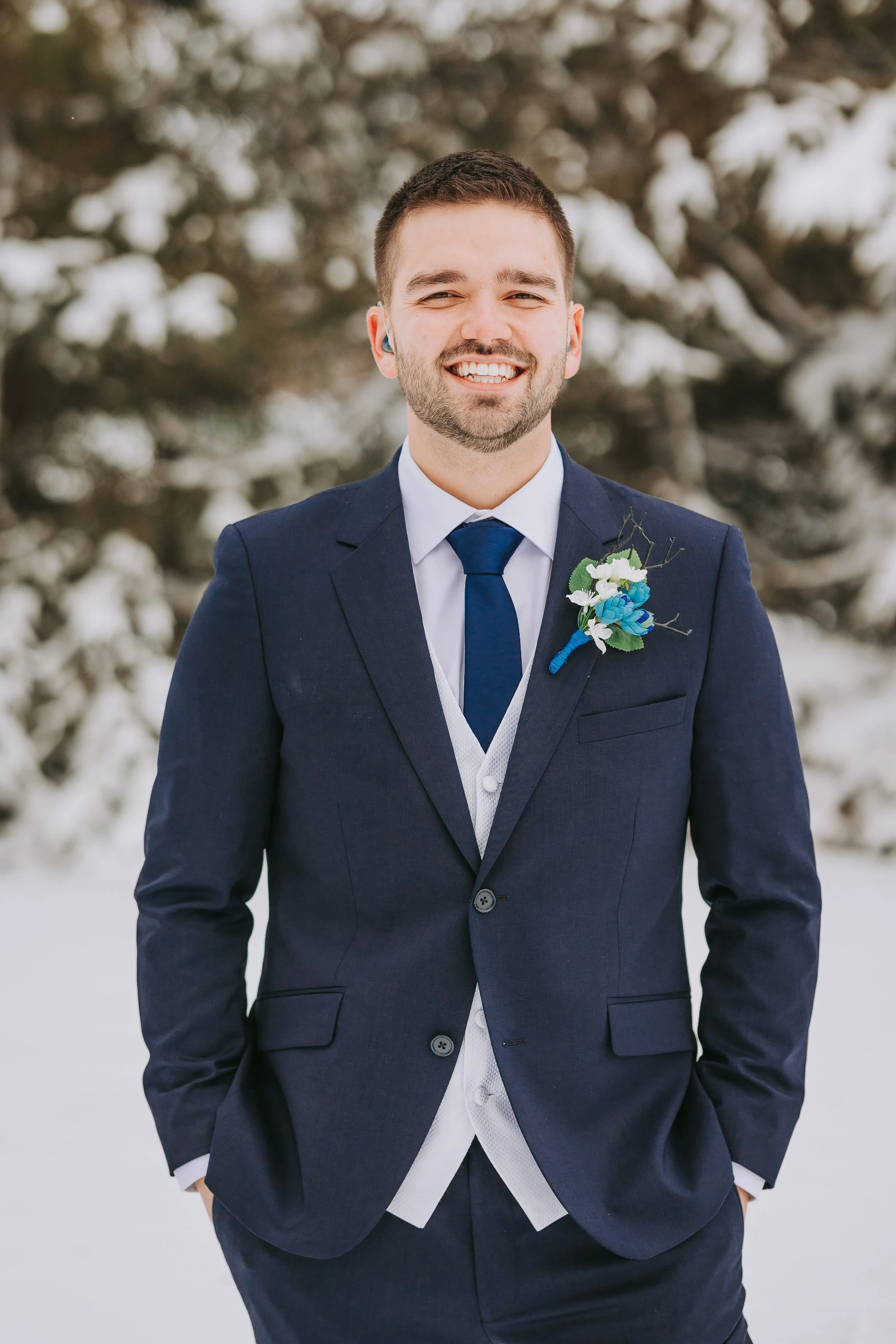 A man in a navy blue suit and tie smiling outdoors in a snowy setting.