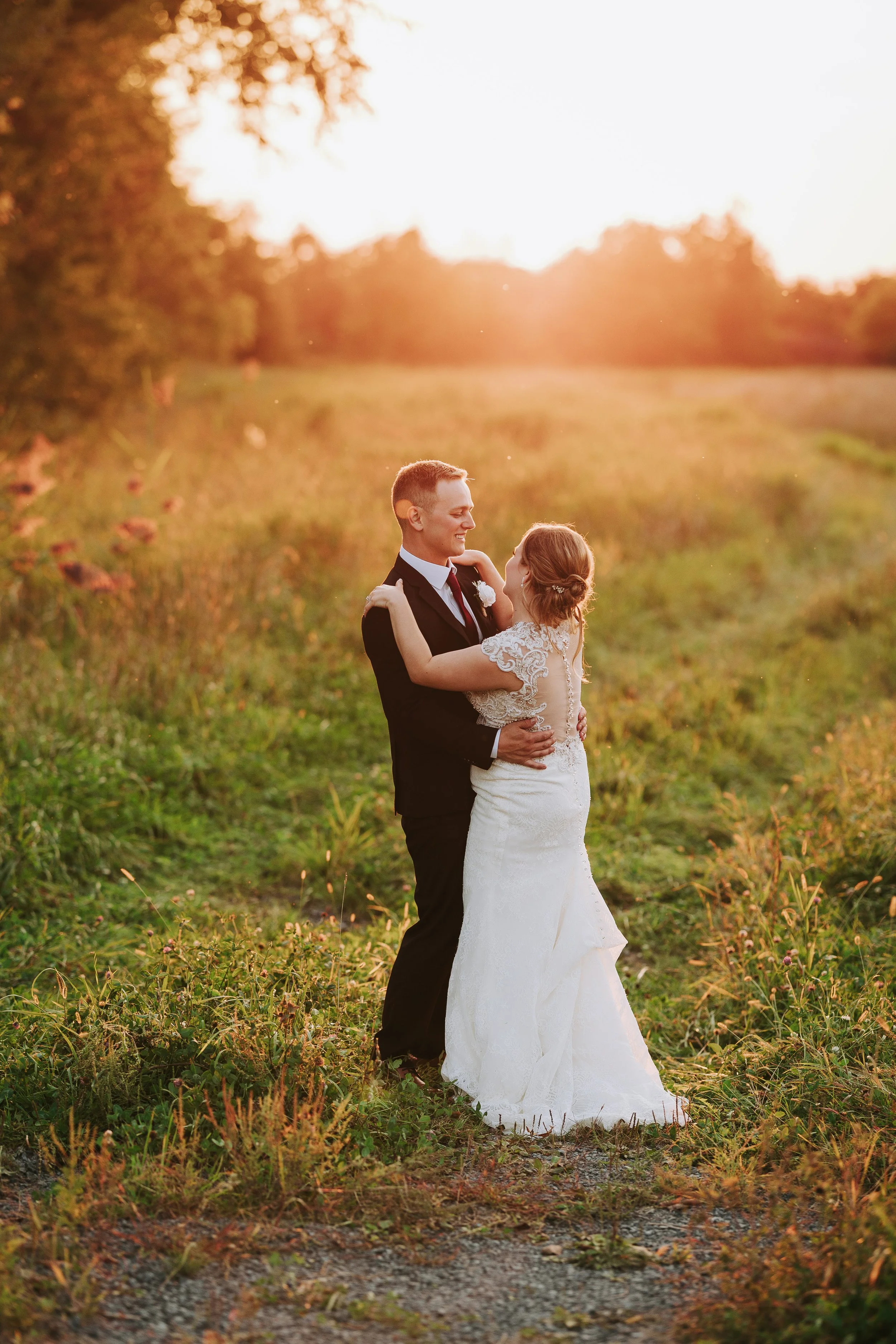 A newlywed couple dancing outdoors at sunset, surrounded by greenery and wildflowers.