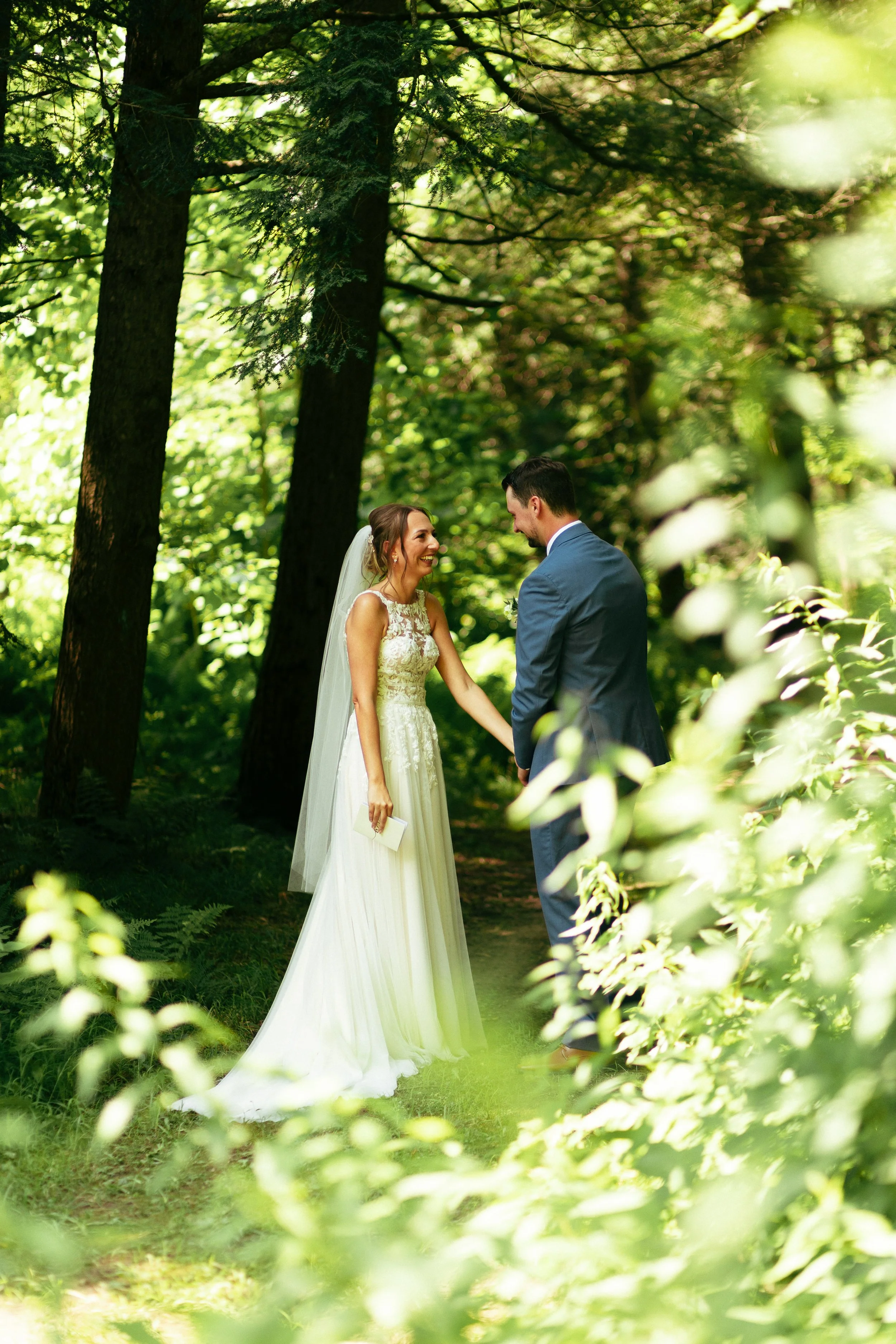 A bride and groom holding hands in a lush green forest, with sunlight filtering through the trees, celebrating their wedding.