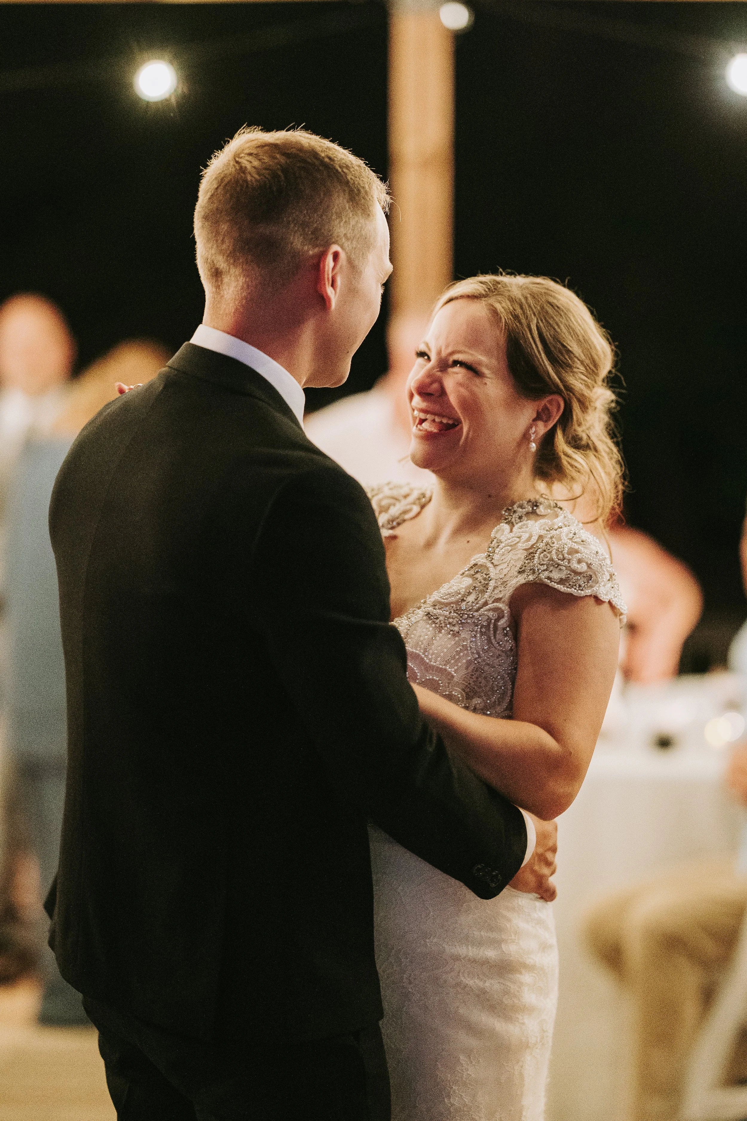 A bride and groom sharing a dance at a wedding reception, looking happy and smiling at each other.