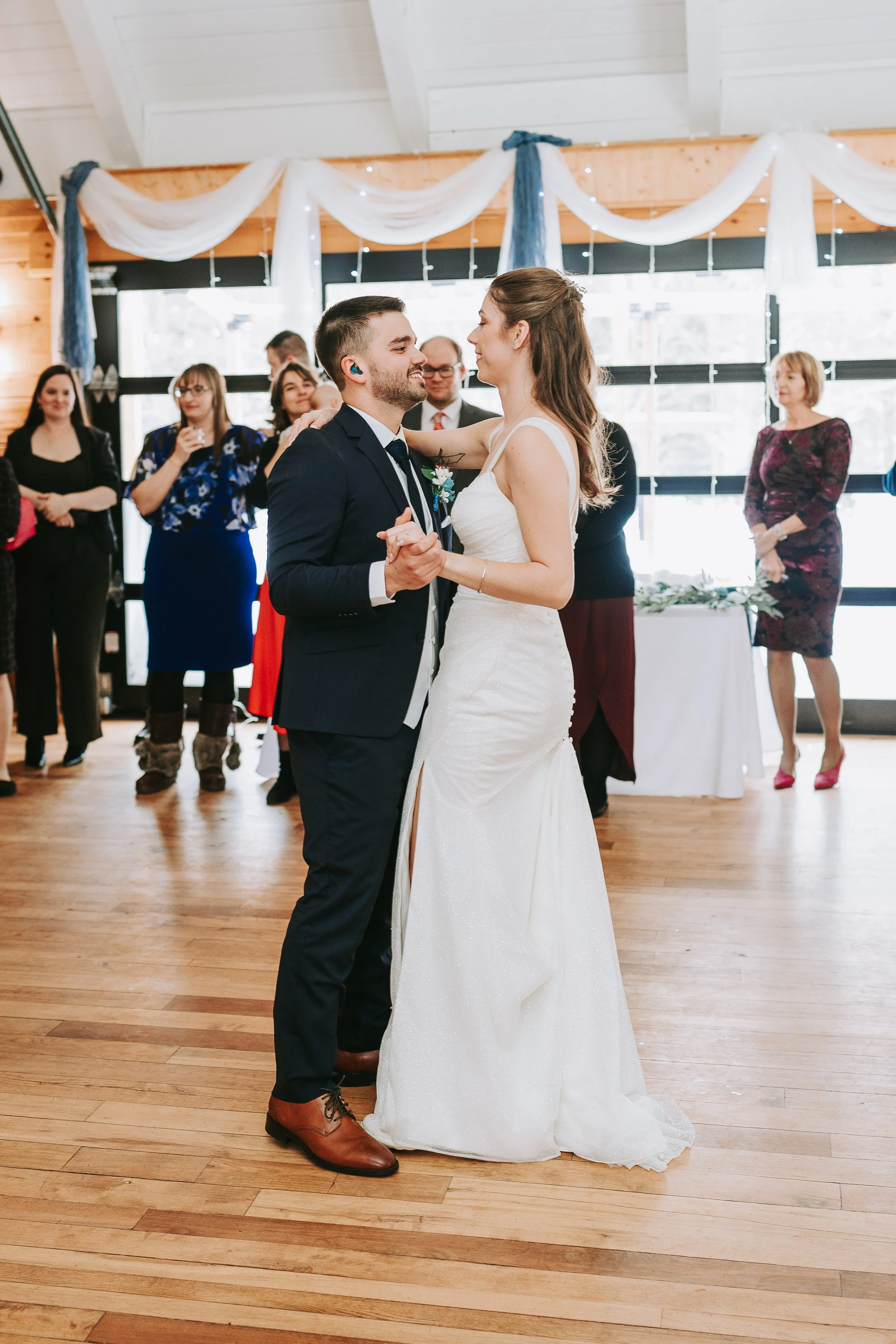 A bride and groom share their first dance at their wedding reception while guests watch.