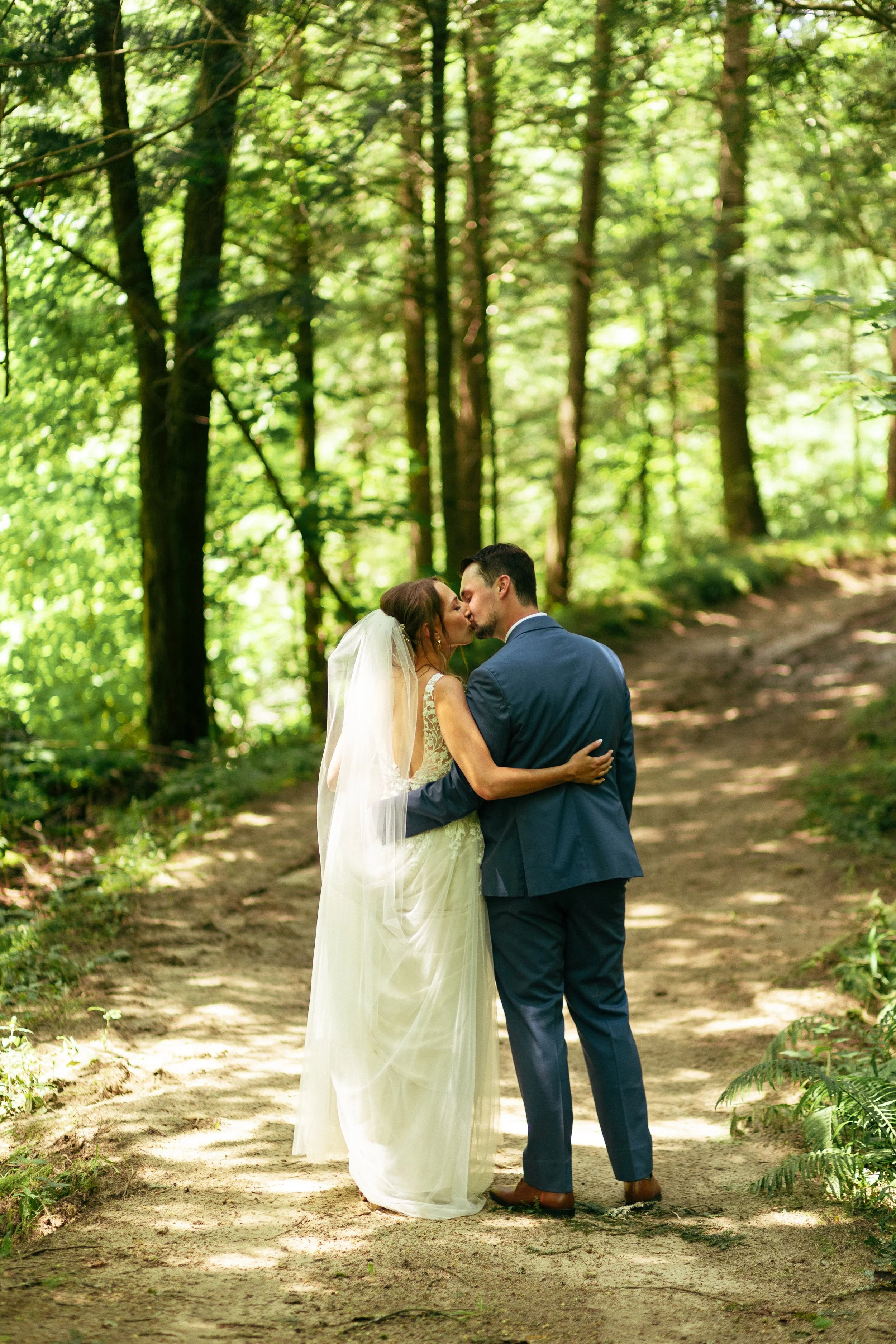 A bride and groom sharing a kiss in a wooded outdoor setting during their wedding.