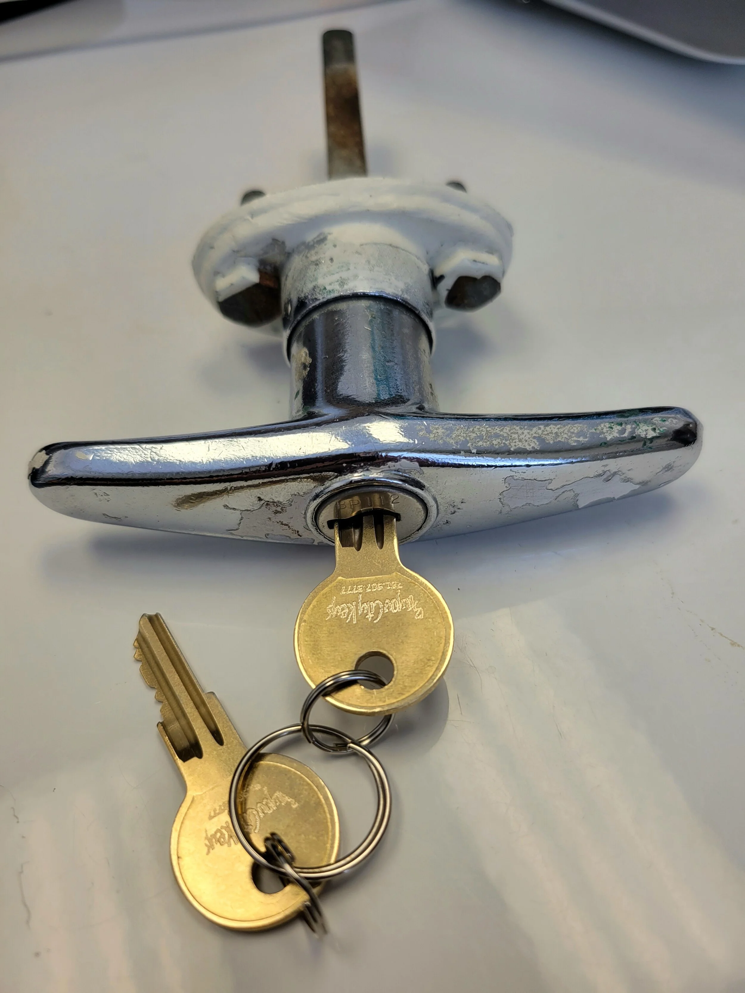 Close-up of a vintage door latch with two keys attached to it on a white surface.