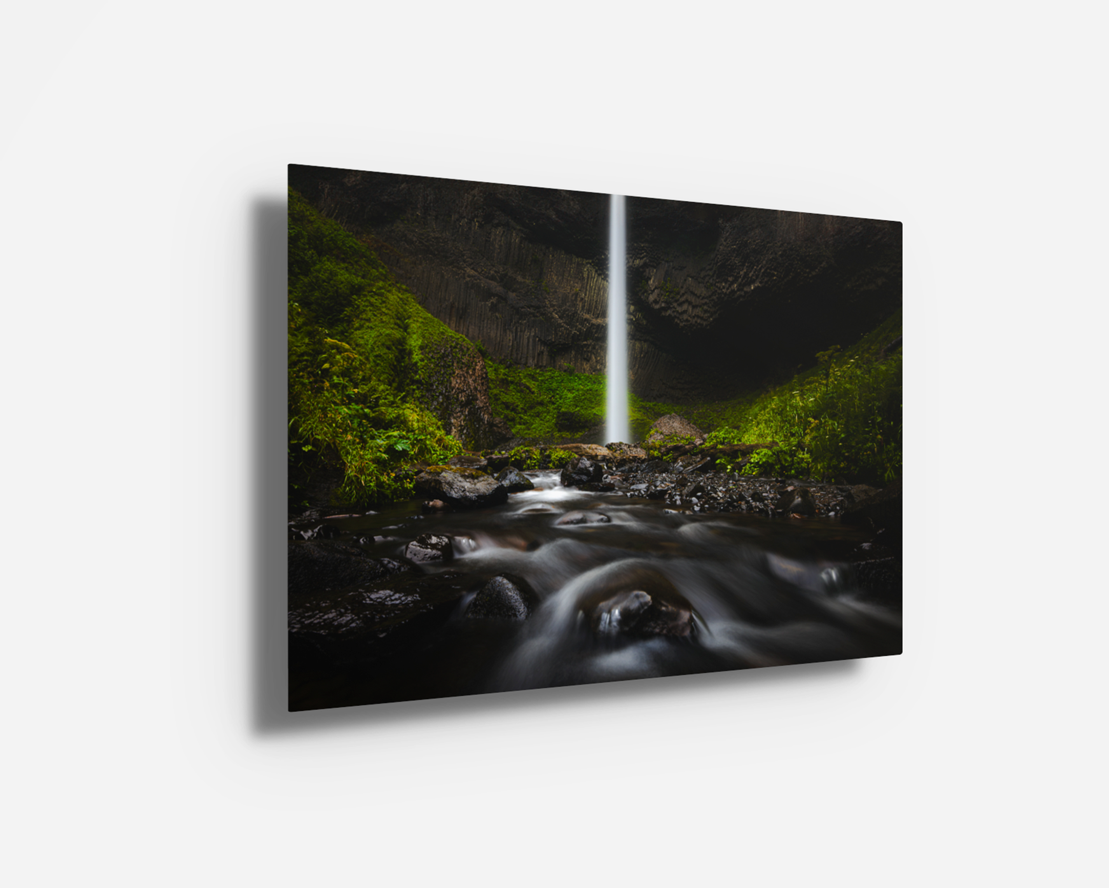 Vibrant metal print of a waterfall against deep basalt walls and glowing green foliage.