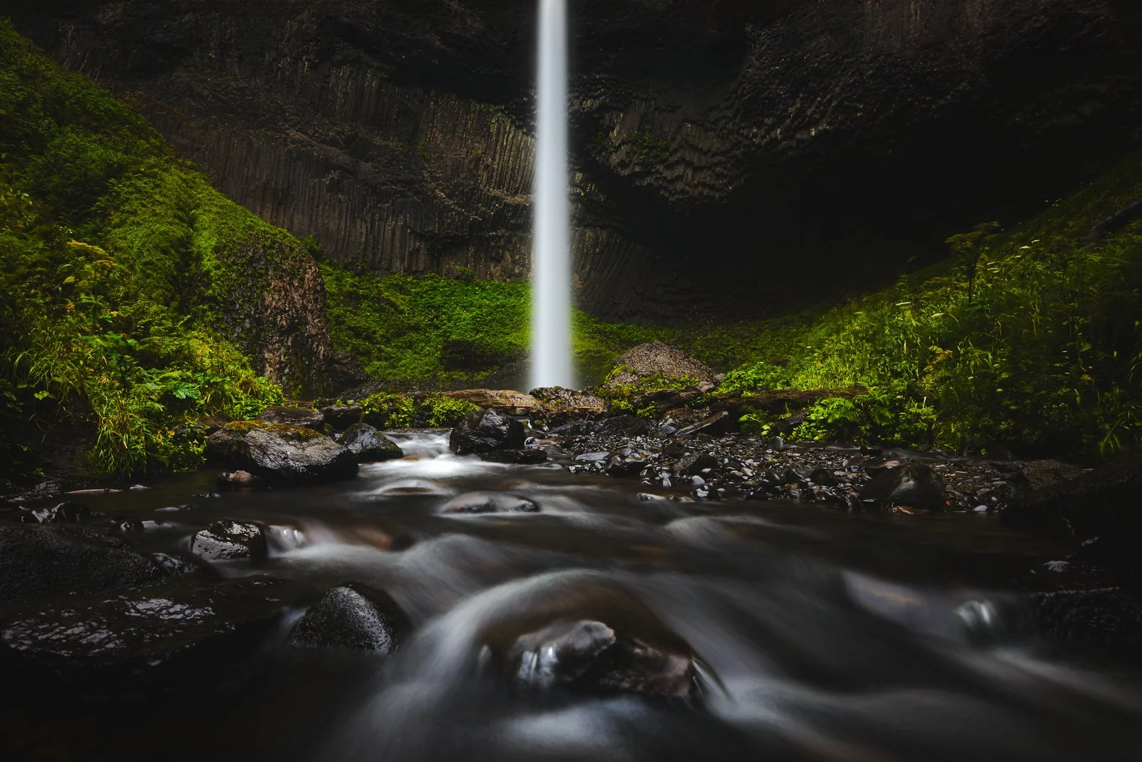 Long exposure of Latourell Falls cascading into a rocky pool, surrounded by vivid green moss and ferns in the Columbia River Gorge.