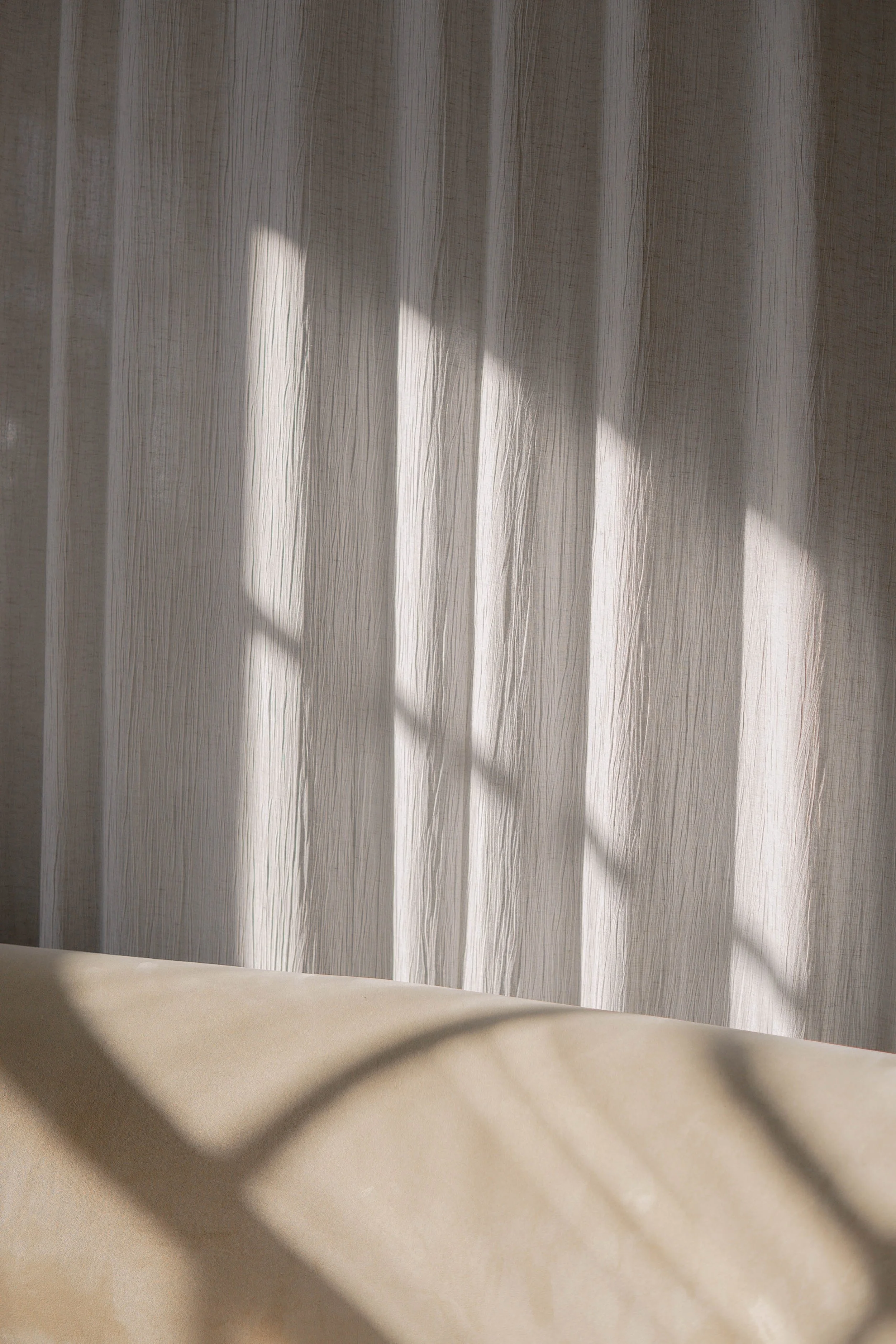 Sunlight casting shadows through a sheer curtain onto a beige surface.