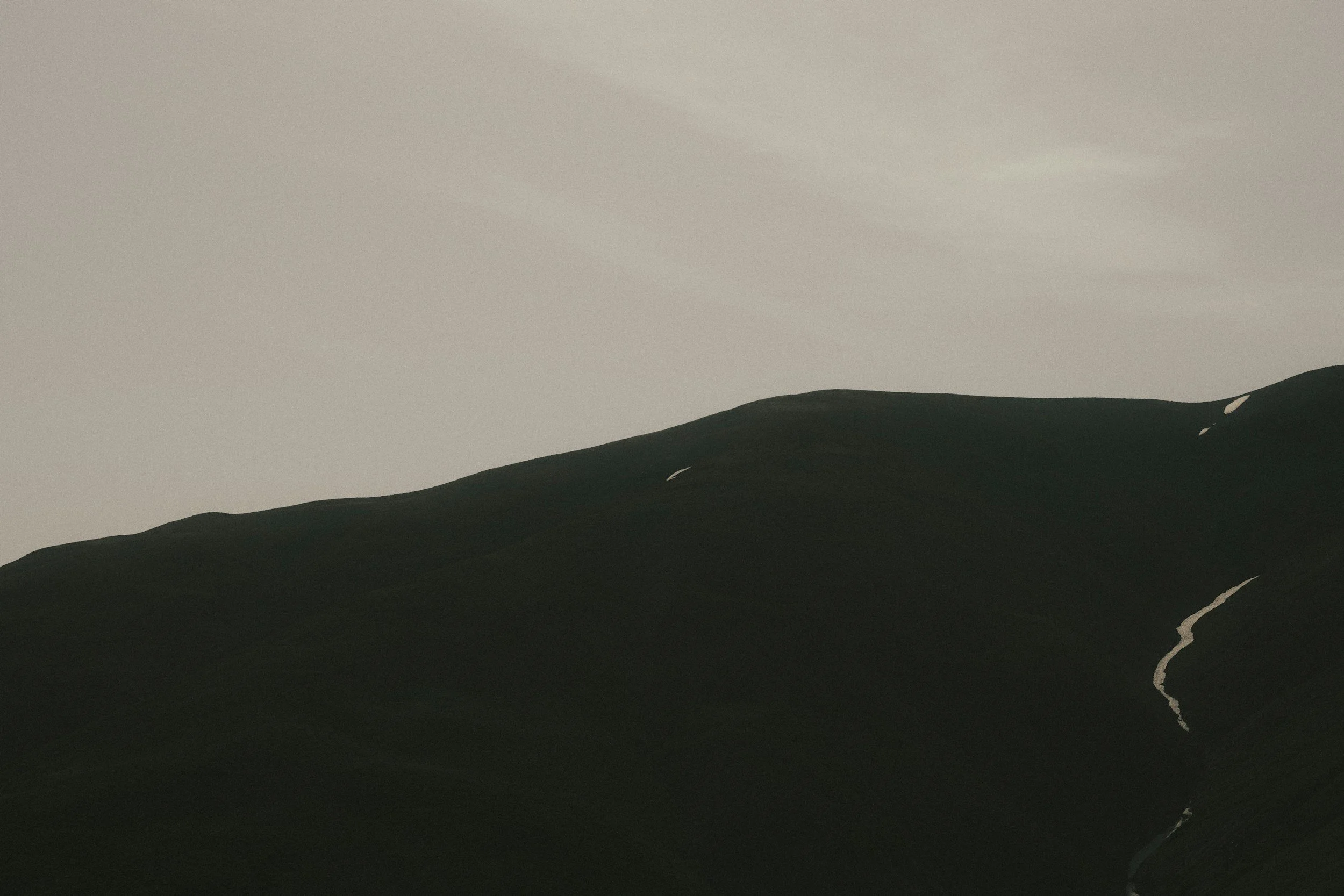 Dark mountain landscape with a light sky and small patches of snow on the peaks.