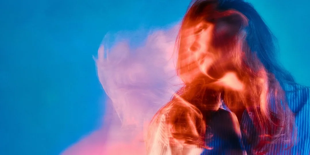 A woman with long dark hair in a pink dress looking at a large crescent moon in the night sky amid a lush, dark forest with lens flare effects.