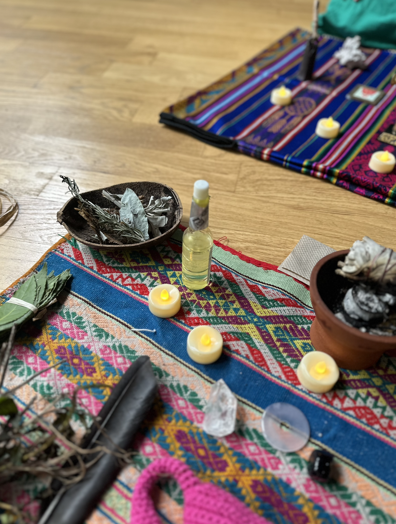 Decorative altar with candles, herbs, crystals, and other ritual items on a colorful woven cloth.