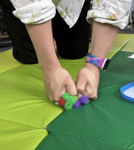 Person kneeling on a colorful mat, holding several small, colorful, spiky balls in their hands.