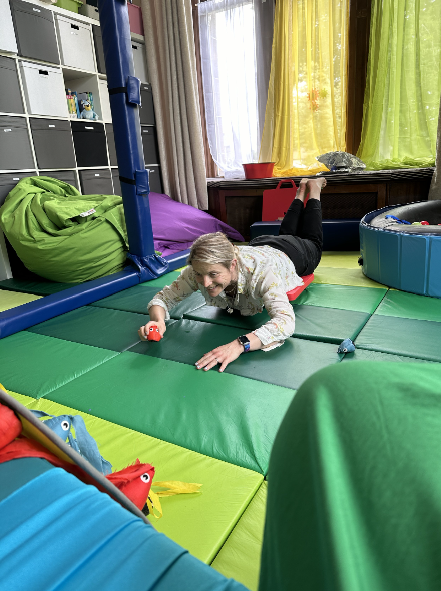 Person playing on colorful padded floor in a playroom with bean bags and shelves in the background.