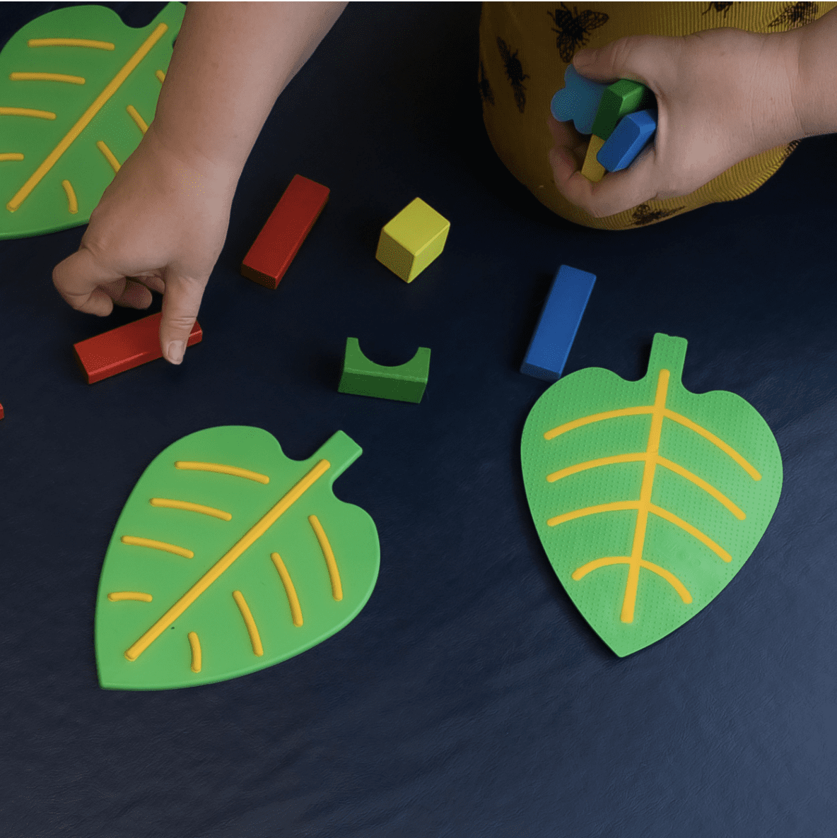 Child playing with colorful blocks and green leaf-shaped toys on a dark surface.