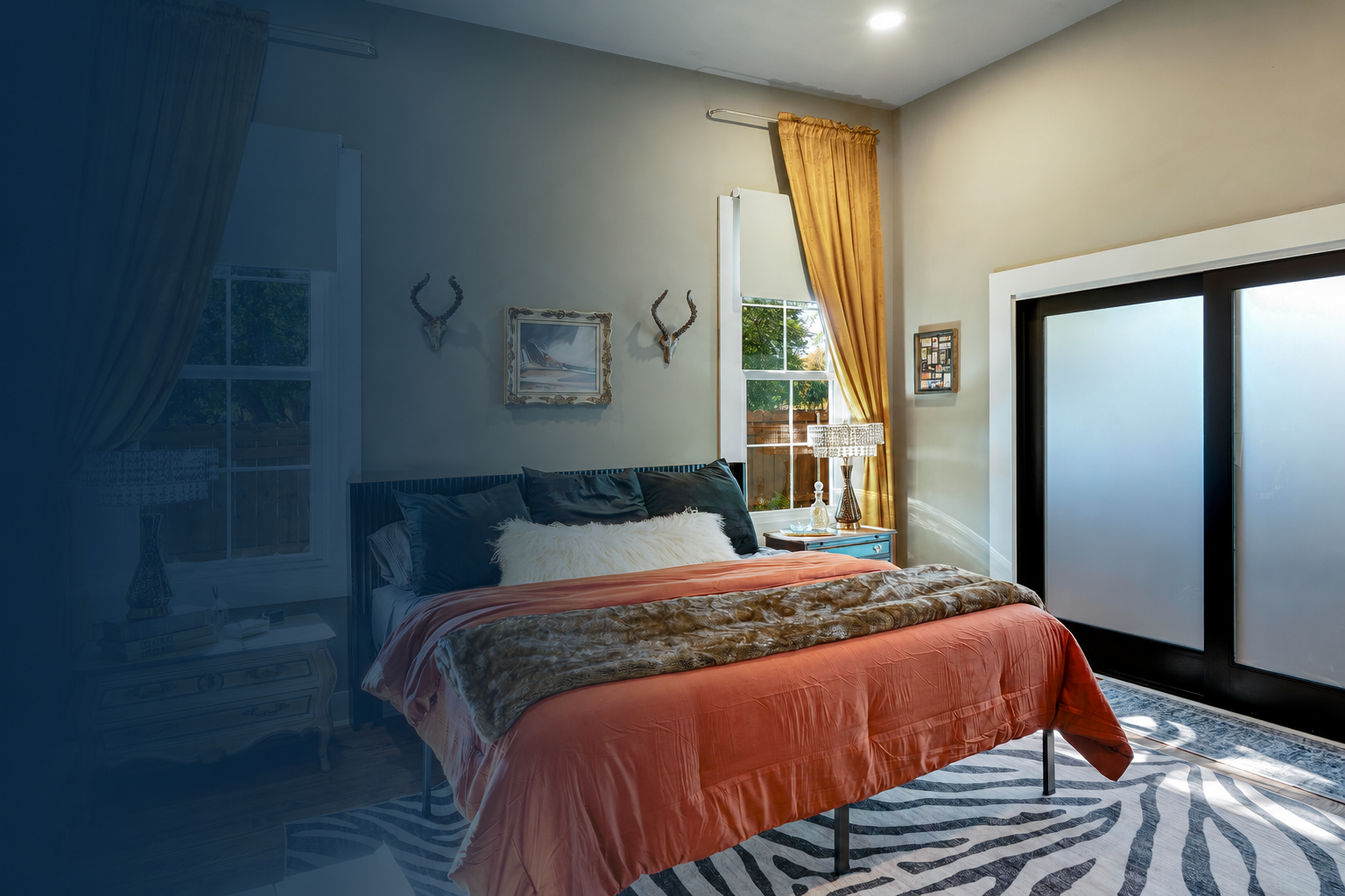 Stylish bedroom with coral bedding, a zebra-patterned rug, wall-mounted horns, and large frosted glass doors.
