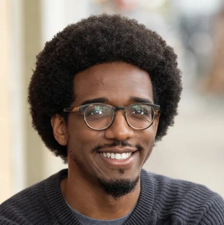 Keane smiling with glasses and an afro