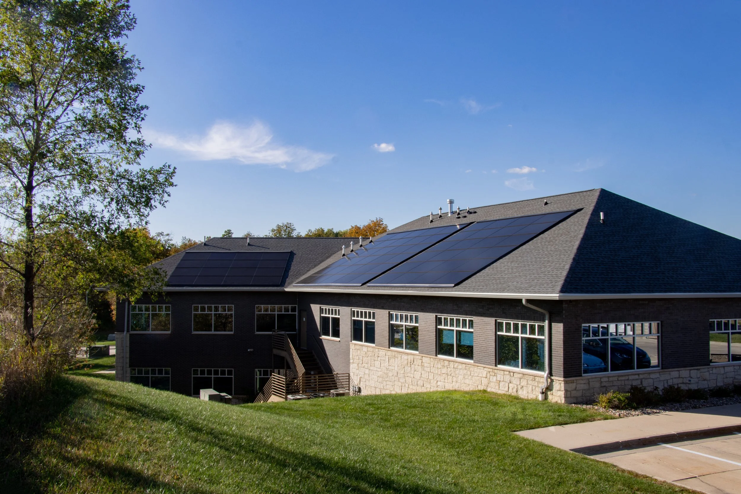 Back view of a home's roof with new solar panels and new roof surrounded by lush green grass and blue skies.