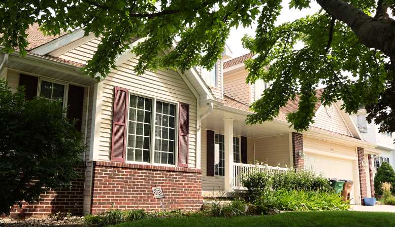 Front view of a house in Ponderosa Dr, West Des Moines with beige siding and brick foundation, surrounded by green trees and plants.