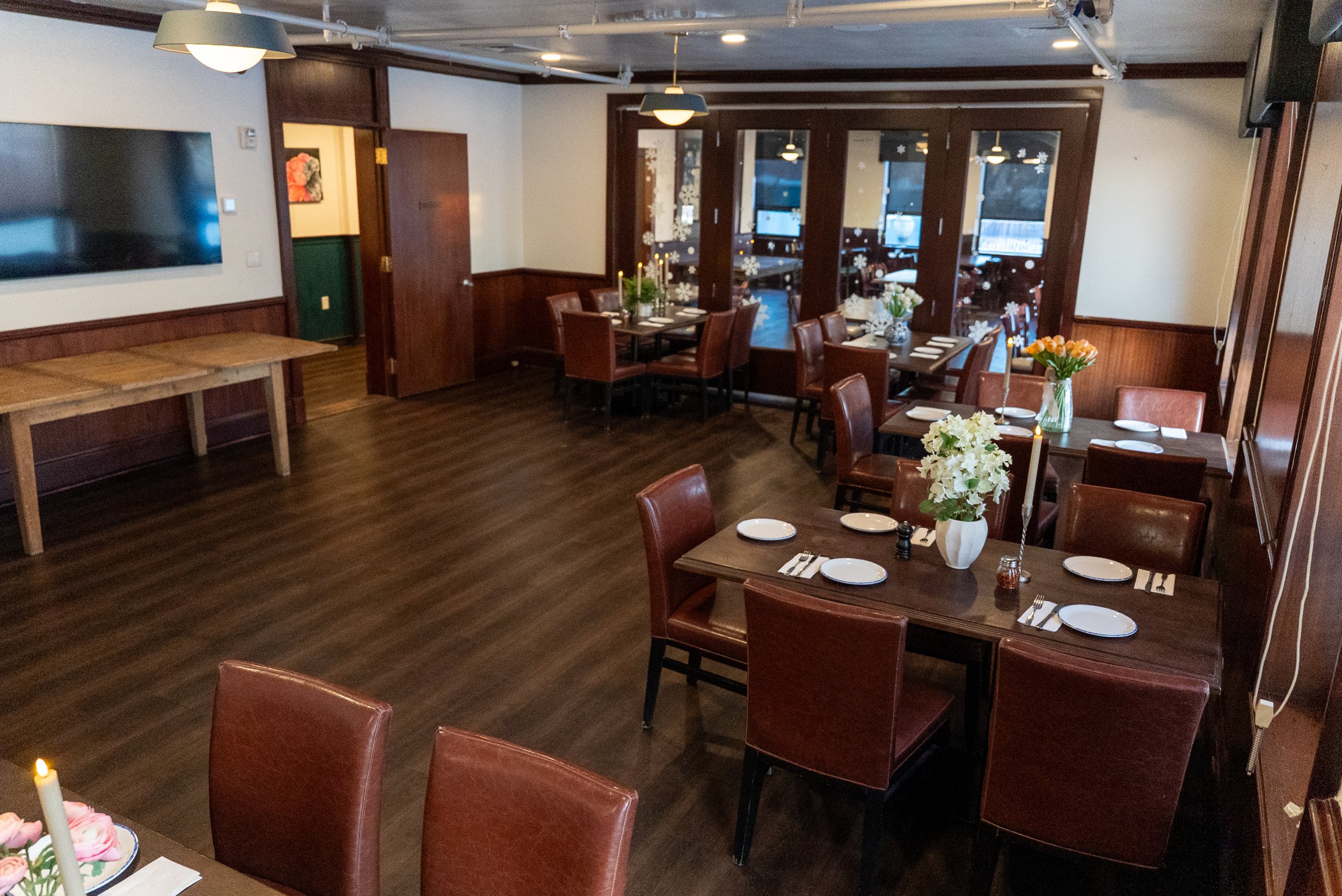 Empty restaurant with dark wooden floors, brown leather chairs, and tables decorated with flowers, candles, and place settings