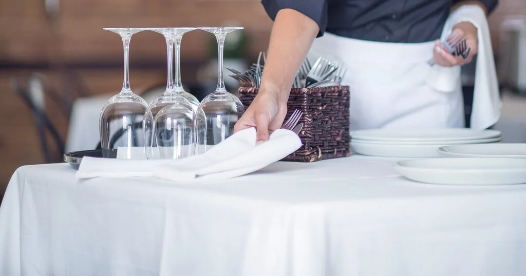 A restaurant server sets a table with clean, crisp linens.