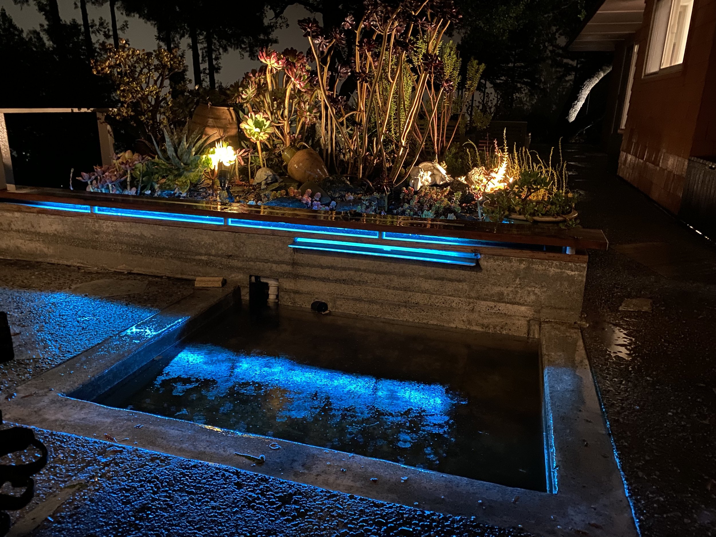Outdoor concrete fountain with LED and water flume, redwood bench on top held by aluminum cylinders