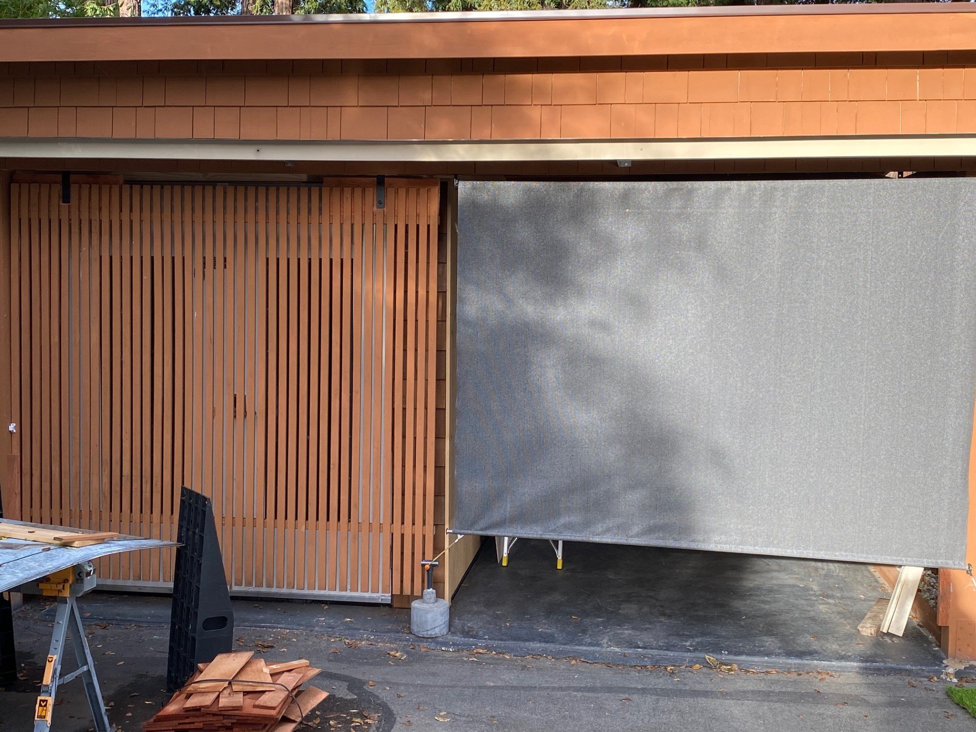 Shed within carport built with old UCSC discarded doors and obscured by wood remnants fashioned into a rolling barn door