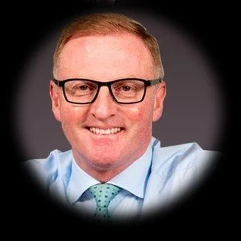 A man with short red hair and glasses wearing a light blue shirt and a green tie that knows the UK's retail payment industry and the leading figures in it and has been at the forefront of the industry for many years.