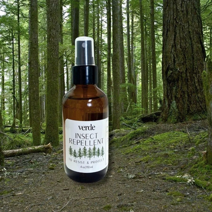 apothecary verde insect repellent bottle in front of a background of a lush, green forest with a path running through the center