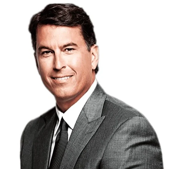 A man in a gray suit and black tie, smiling, with short dark hair and fair skin.