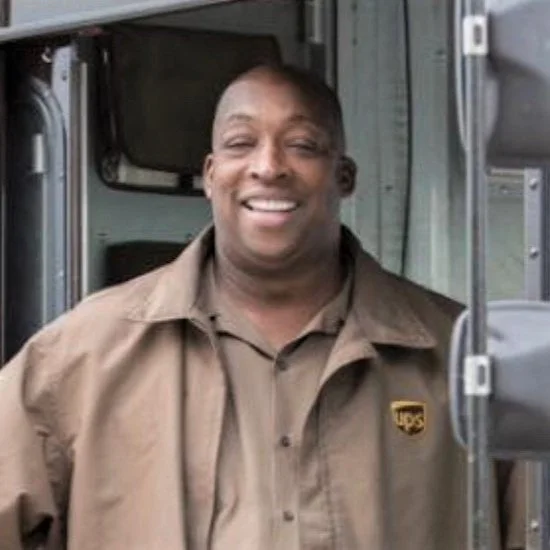 A smiling man in a brown uniform standing next to a food truck.