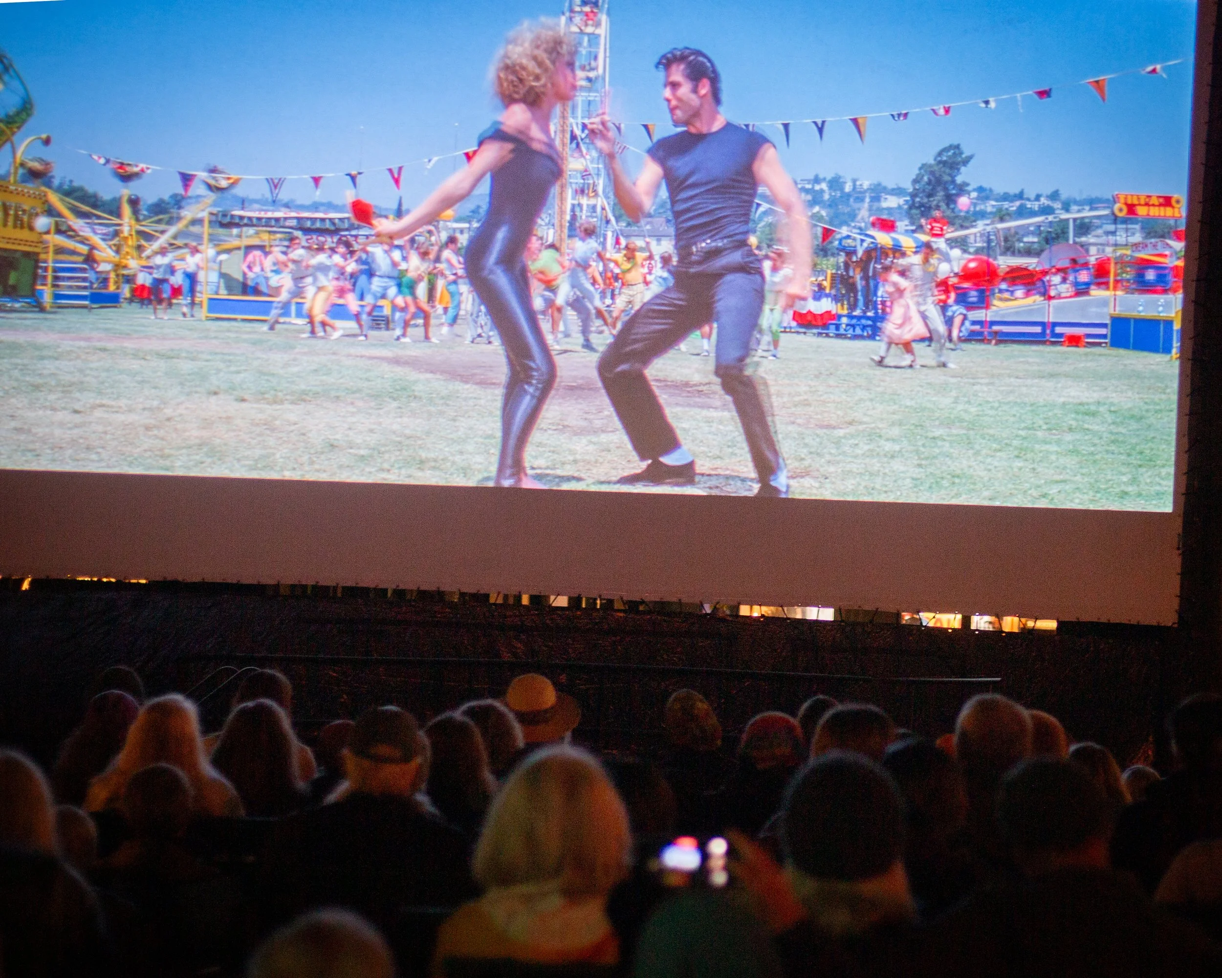 A projection shows a scene from a carnival or fair, featuring a dancing man and woman in the foreground with a crowd and amusement rides in the background.