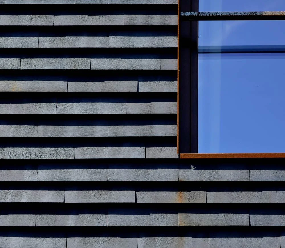 SKALA K clay shingle facade in dark slag color showing layered C-shaped profile, shadow lines, and ventilated rainscreen cladding detail around window opening.