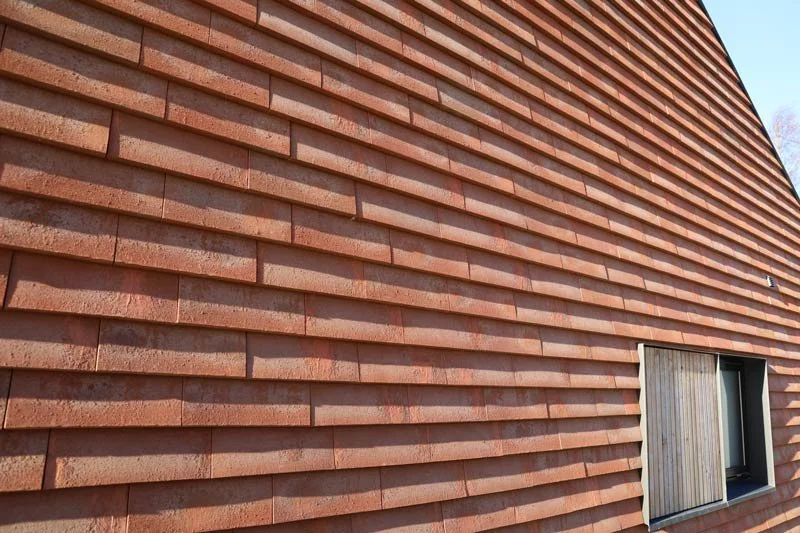 SKALA K brick clay shingles installed on exterior facade showing C-shaped profile, natural clay texture, and horizontal rainscreen layout in brick color.