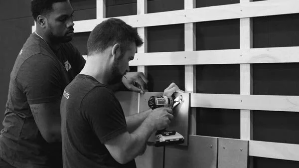 Two workers installing SKALA panels on a wooden framework using a power drill, demonstrating the ease of installation.