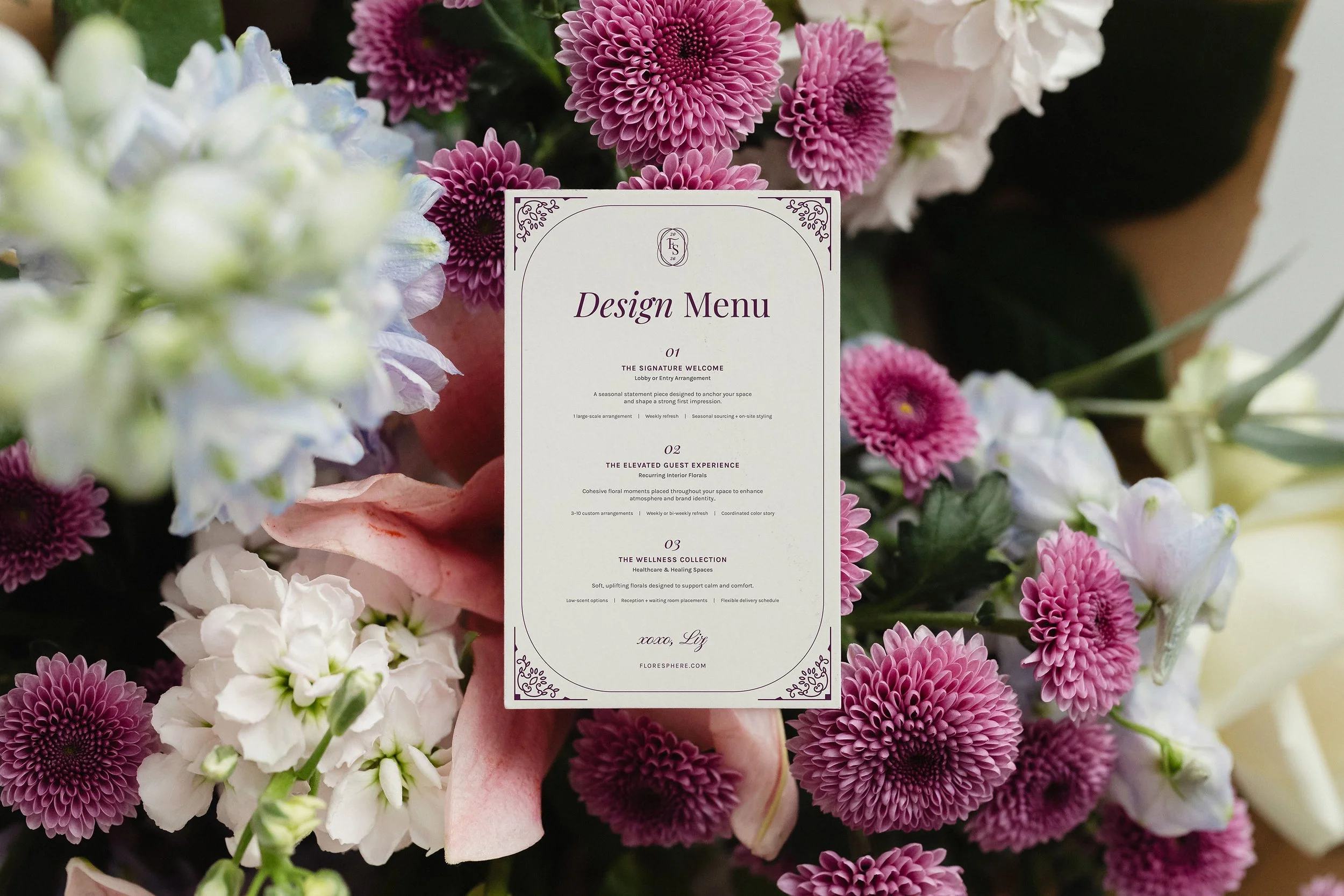 A floral arrangement with pink, purple, white flowers surrounding a white event design menu card.