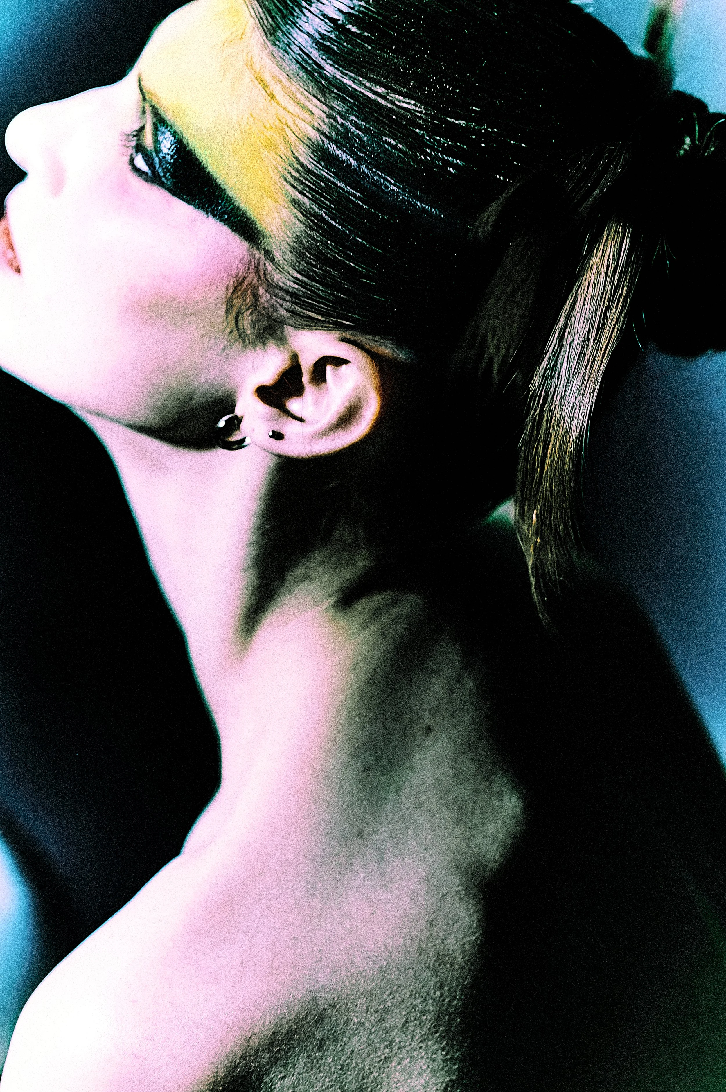 A close-up of a woman's face in profile, with colorful makeup and dark, straight hair styled in an updo.