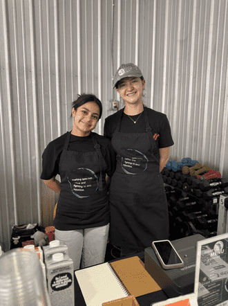 two baristas with aprons on standing behind a counter and smiling