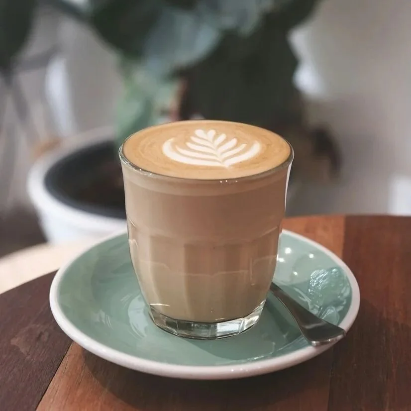 a cappuccino in a glass cup on top of a blue plate on a wooden table.