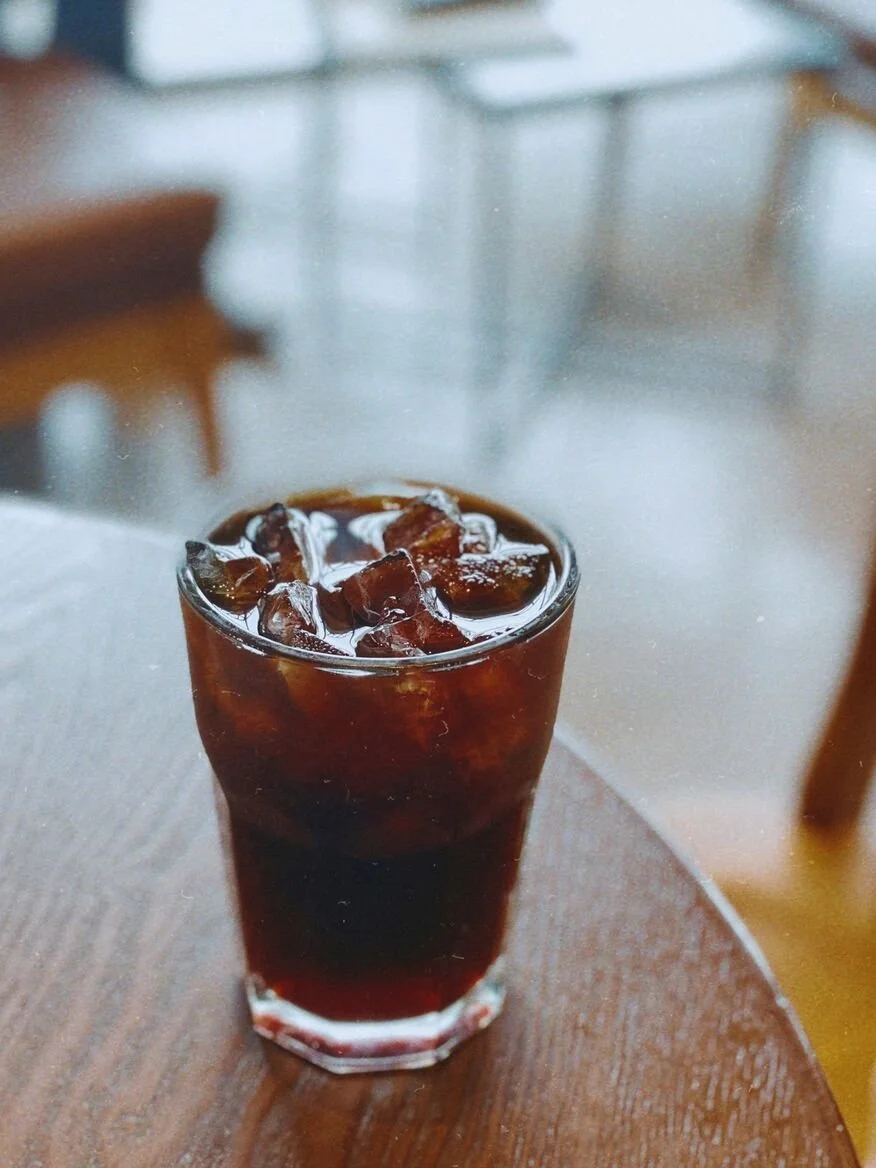 an iced americano in a glass cup sitting on top of a wooden table.