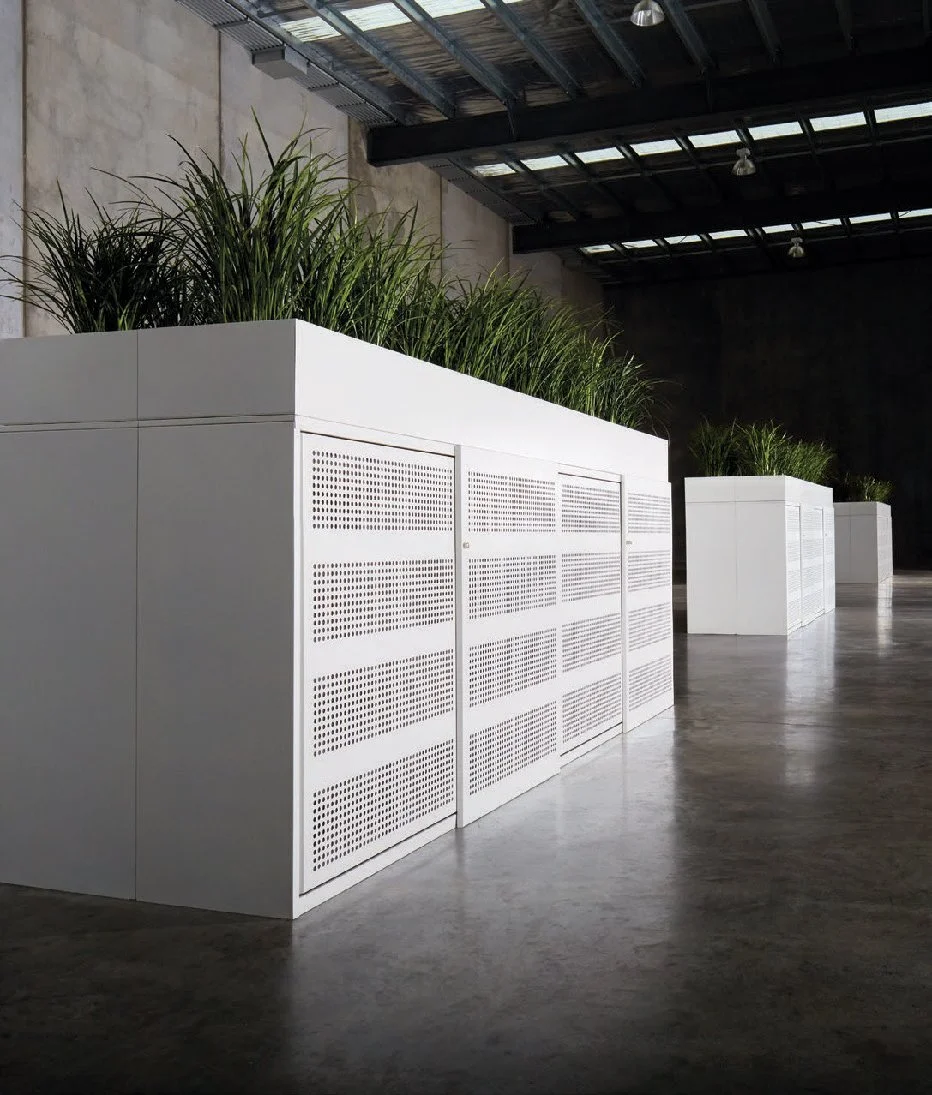 Indoor industrial space with white planters filled with green grass, metal roof, concrete floor, and a high ceiling.
