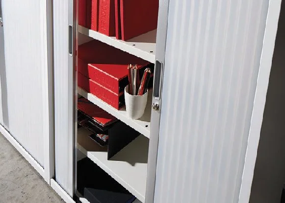 White storage cabinet with sliding doors, containing red binders, a white cup with pens and pencils, and some black and red files.