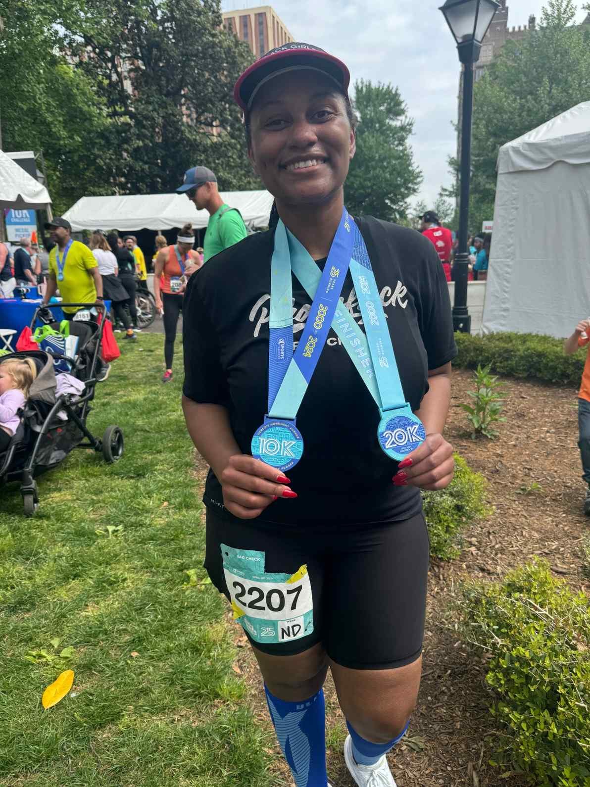 Black female runner holding up her medals after her race.