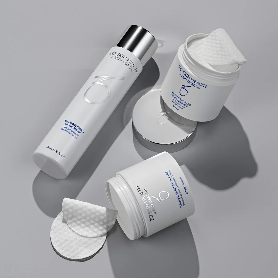 Skincare products, including a toner, cotton pads, and a jar of cleansing pads on a light gray surface