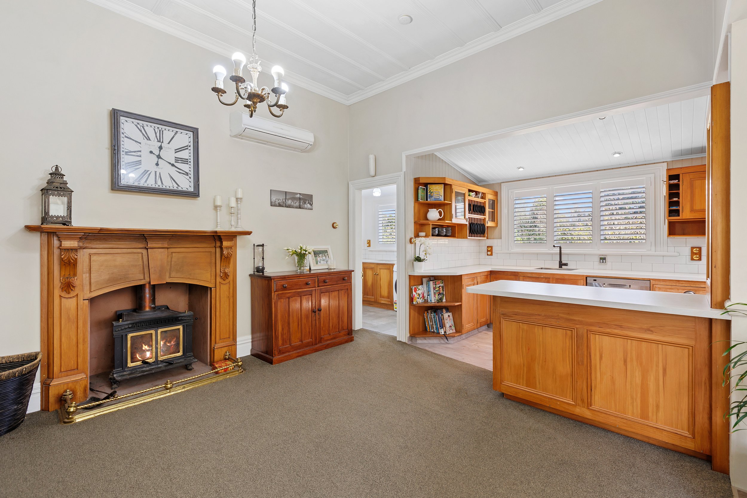 Living room with fireplace, wooden furniture, open kitchen, and large wall clock.