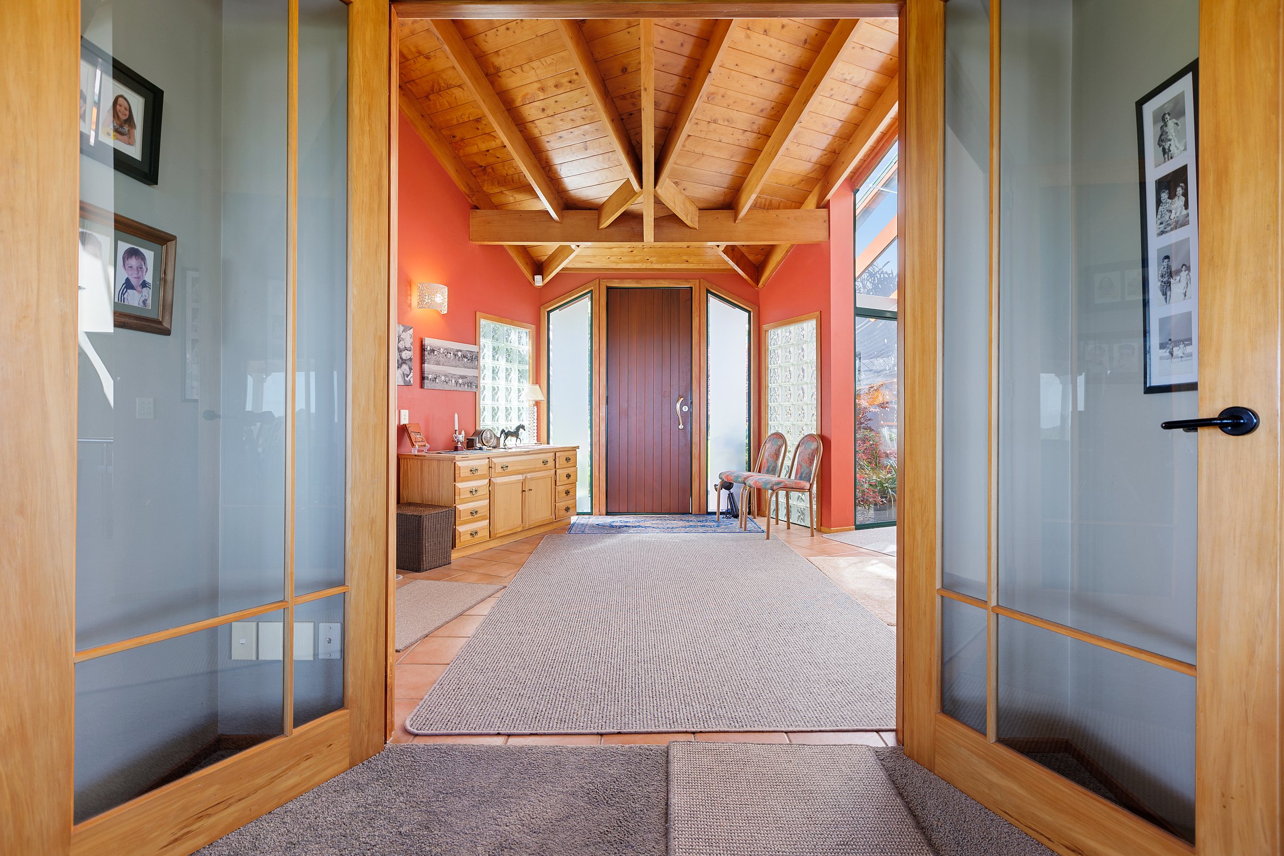 Interior entryway with wooden ceiling, red walls, glass doors, carpeted floor, wooden furniture, and framed photos.