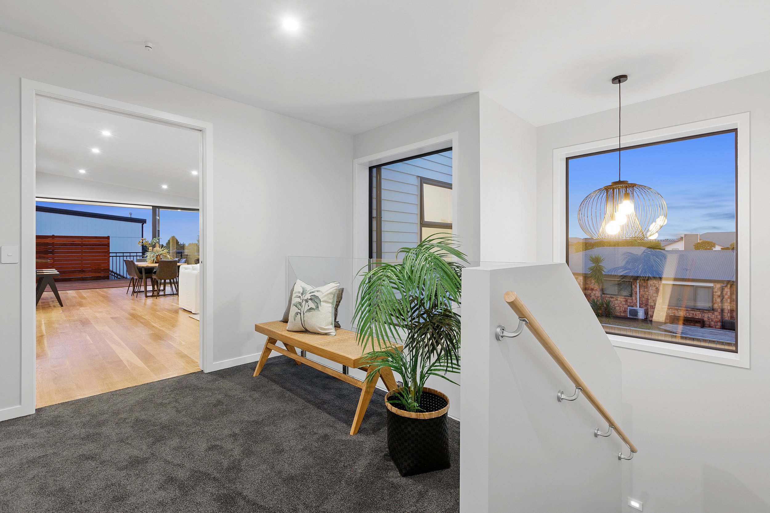 Modern interior with wooden bench, plant, and pendant light, leading to a dining area with balcony views.