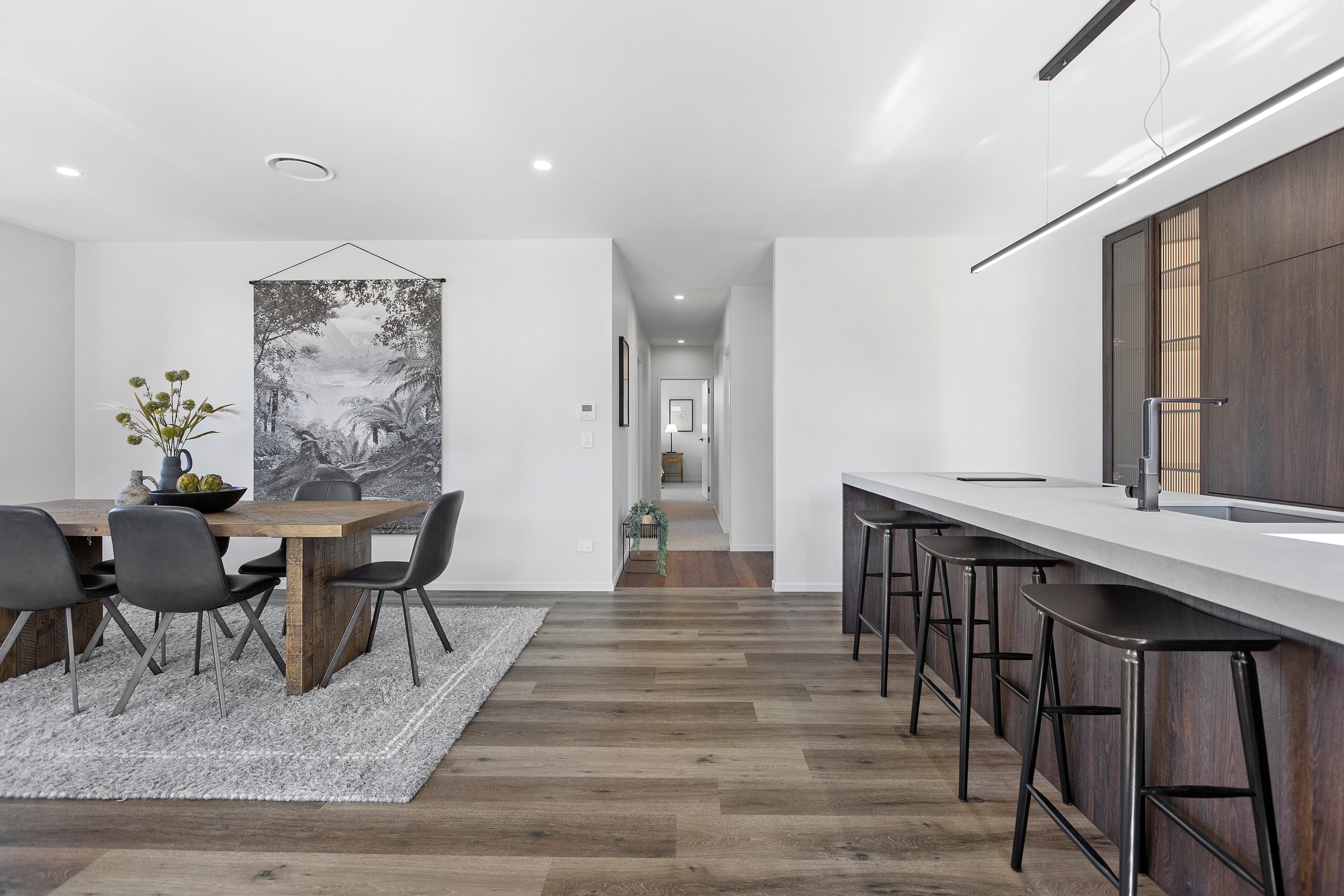 Modern dining and kitchen area with a wooden dining table, black chairs, large wall art, and a sleek kitchen island with bar stools.