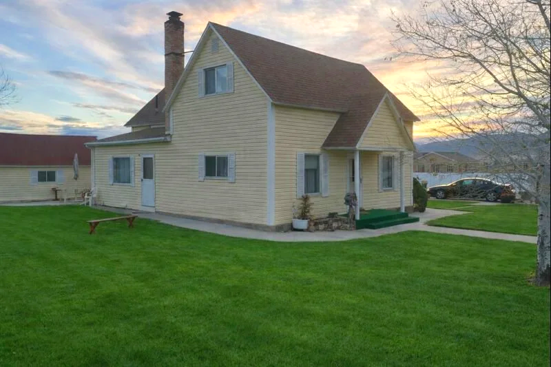 McKay Jensen childhood home surrounded by a green lawn and a tree, with a sunset sky in the background.