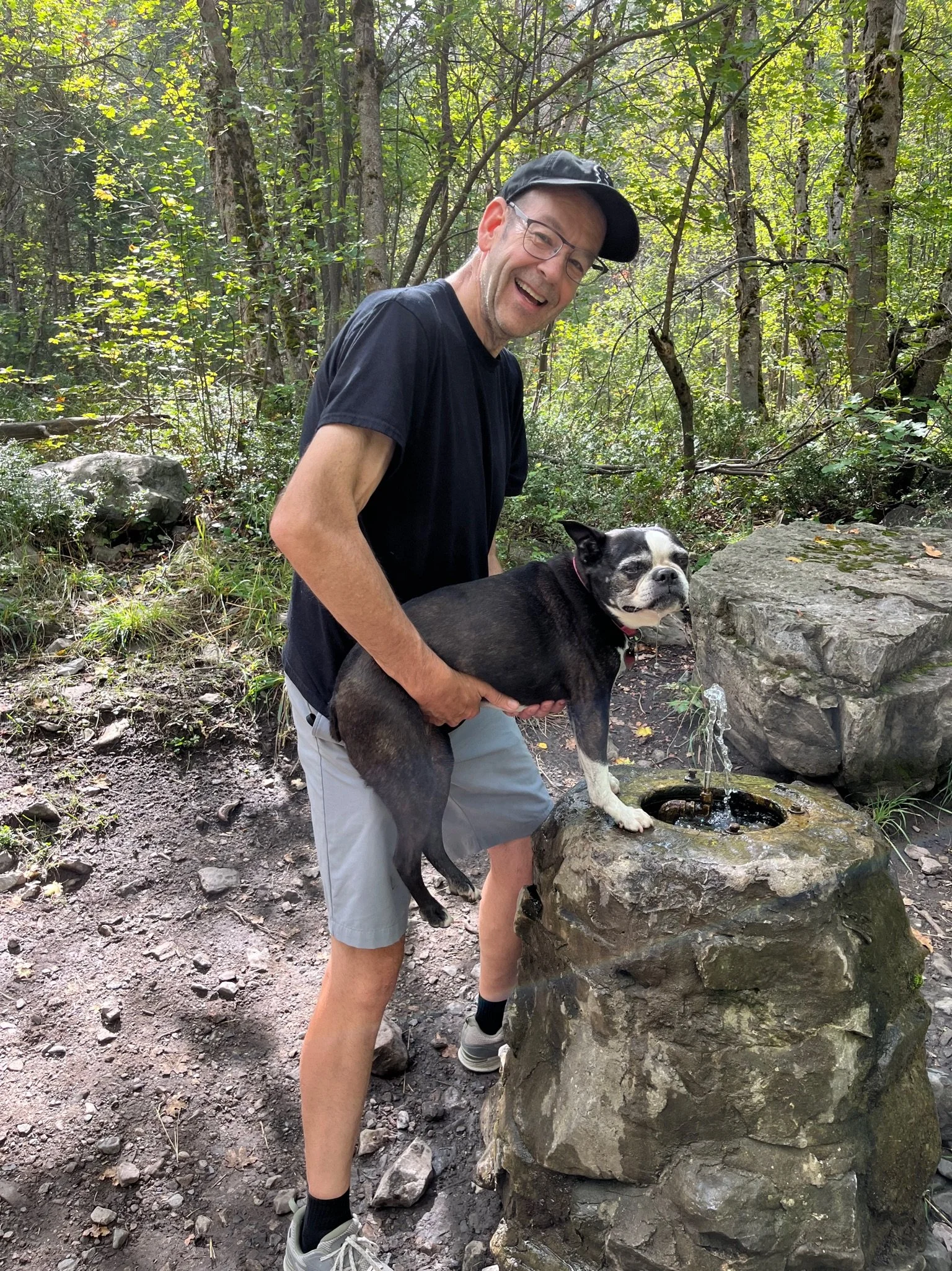 McKay Jensen with Dot the dog at a forest trail with a small water fountain on a rock.