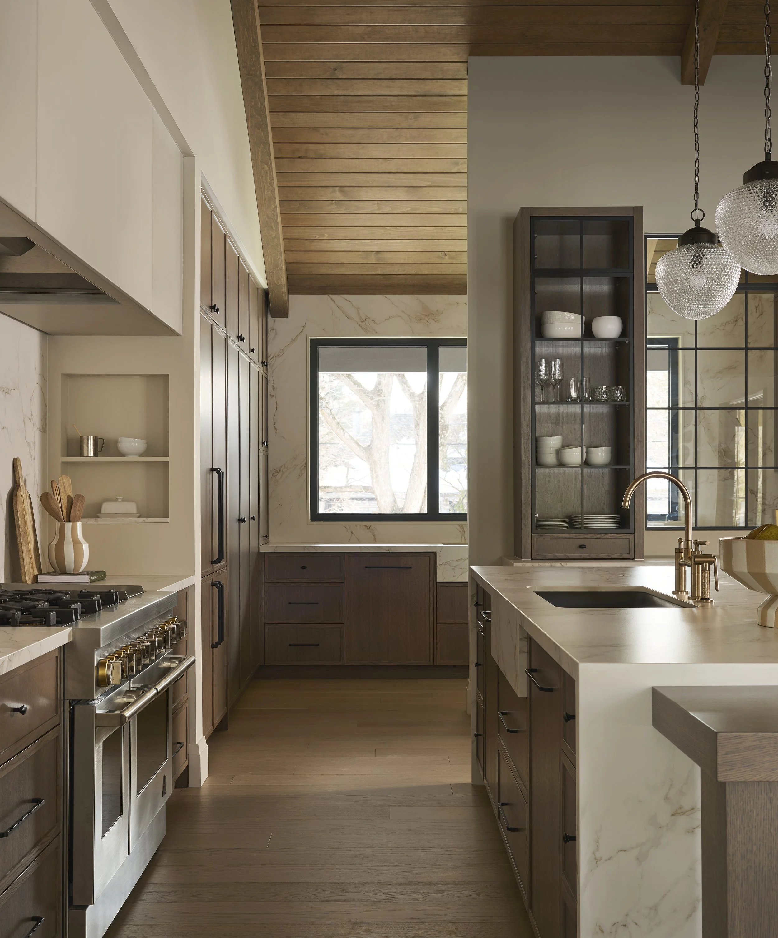 Modern custom built kitchen with wooden cabinets, marble countertops, a window, and hanging light fixtures.